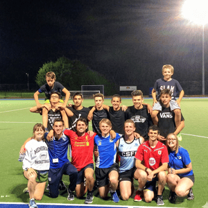 Equipo de estudiantes de InterWay posando eufóricos y abrazados en el campo deportivo iluminado tras un partido nocturno en Bath College.