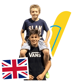 Dos estudiantes del curso de inglés en Bath College de InterWay sonriendo, con un alumno a hombros de otro, junto a la bandera del Reino Unido