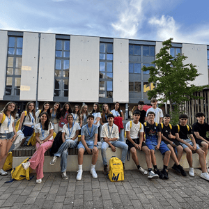 Grupo de estudiantes del curso de inglés en Bath de InterWay posando juntos con sus mochilas amarillas en la plaza exterior del campus residencial.