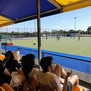 Estudiantes de InterWay sentados en las gradas cubiertas observando un entrenamiento en las instalaciones deportivas al aire libre del campus de Bath.