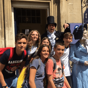 Grupo de alumnos de InterWay posando sonrientes en Bath junto a un actor disfrazado de época georgiana durante una actividad turística y cultural.