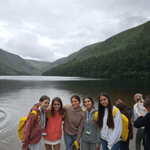 Alumnas del programa de idiomas de InterWay con mochilas amarillas posando juntas durante una excursión de naturaleza al lago de Glendalough en Irlanda.