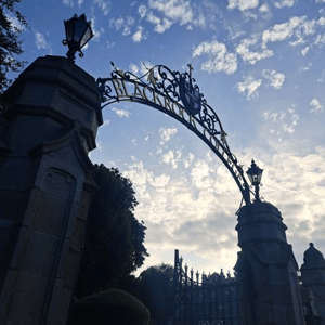 Vista en contrapicado de la histórica puerta arqueada de hierro forjado con farolas en la entrada del campus residencial