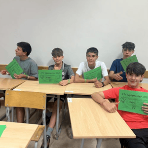 Un grupo de alumnos varones sentados en los pupitres de clase mostrando orgullosos sus proyectos o certificados en cartulinas verdes durante el curso de InterWay en Dublín.