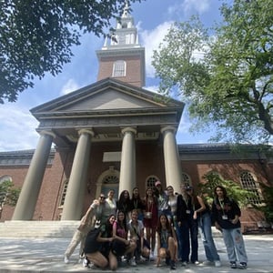 Un grupo de jóvenes alumnos de InterWay posa sonriente frente a un edificio académico clásico de ladrillo con columnas y torre de reloj en Boston.