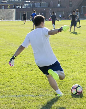 Un joven jugador de espaldas golpea un balón de fútbol sobre el terreno de juego durante un partido organizado en el campus de verano de InterWay en Boston.
