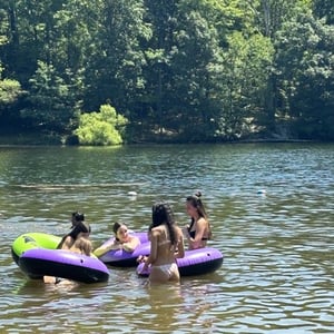 Alumnas del programa de Boston de InterWay disfrutando de una divertida actividad de verano flotando en flotadores gigantes sobre un río rodeado de árboles.