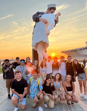 Un grupo de alumnos de InterWay posa al atardecer frente a la gran estatua conmemorativa del beso del marinero y la enfermera (Unconditional Surrender) en la costa de California.
