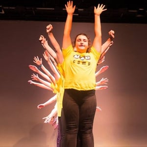 Una estudiante actuando en el centro del escenario mientras el resto de alumnos alineados detrás despliegan sus brazos en abanico durante la obra de teatro de InterWay en Irlanda.