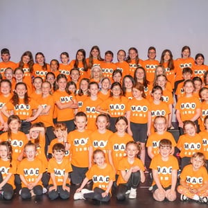 Gran foto de grupo con todos los estudiantes del curso de teatro y actuación de InterWay en Irlanda posando juntos con camisetas naranjas sobre las gradas.