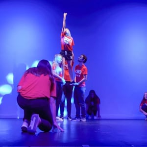 Alumnos del programa artístico de InterWay realizando una figura acrobática y una torre humana en un escenario iluminado con focos azules.