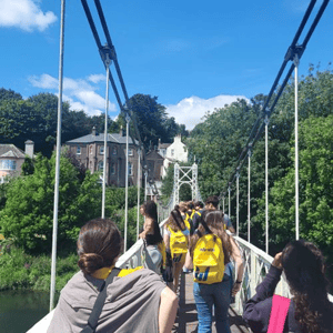Estudiantes del programa de verano de InterWay con mochilas amarillas cruzando el puente colgante de Daly's Bridge (Shakey Bridge) sobre el río Lee en Cork.