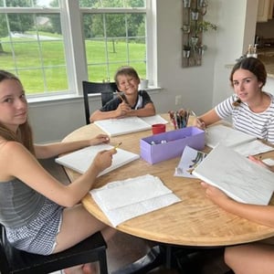 Tres alumnas del curso de InterWay concentradas haciendo tareas o manualidades sentadas en la mesa de madera de un comedor americano.