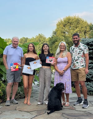 Alumnos del programa de verano de InterWay y su familia de acogida americana posando sonrientes en un jardín exterior con un perro de color negro.