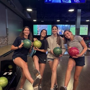 Cuatro estudiantes del viaje de idiomas de InterWay posan sonrientes sujetando bolas de bolos dentro de una bolera americana.