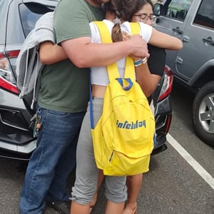 Un emotivo abrazo entre un estudiante y un miembro de su familia de acogida estadounidense en Denver, con una mochila amarilla de InterWay.