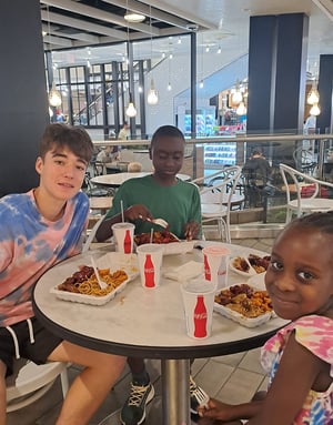 Tres estudiantes del programa en EE. UU. de InterWay compartiendo una comida animada alrededor de una mesa redonda en un local o cafetería.