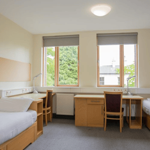Habitación de estudiantes en una residencia del programa de idiomas de InterWay, equipada con escritorios de madera orientados hacia ventanas con vistas exteriores.