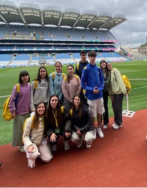 Grupo de estudiantes del curso de inglés Discover Dublin de InterWay posando juntos en la pista del estadio Croke Park, con las gradas azules y el campo de césped de fondo.