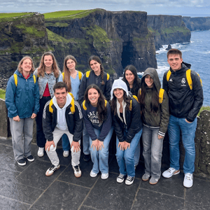 Grupo de estudiantes y jóvenes posando juntos durante una excursión en los acantilados de Moher, Irlanda, con el océano de fondo en un día nublado.