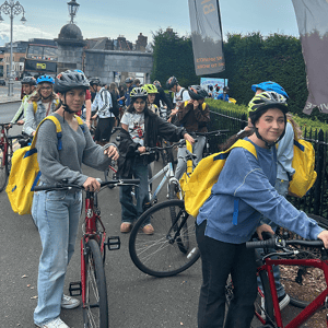Estudiantes con cascos de protección y mochilas amarillas preparándose para una ruta guiada en bicicleta por la ciudad.