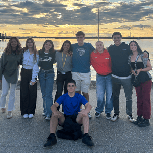Grupo de amigos posando sonrientes en un paseo marítimo junto al agua durante un atardecer dorado.
