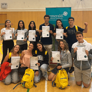 Estudiantes internacionales posando orgullosos en un pabellón mientras muestran sus diplomas de graduación frente a un cartel de Emerald Cultural Institute.