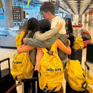 Un grupo de jóvenes con mochilas amarillas brillantes se abraza en la zona de recogida de equipajes de un aeropuerto al final de su viaje.