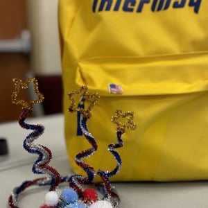 Detalle de una mochila escolar de color amarillo corporativo de InterWay en una sala interior junto a pequeños elementos decorativos.
