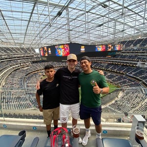 Tres estudiantes del programa de InterWay posan en la zona alta de las gradas de un inmenso estadio cubierto durante una excursión.