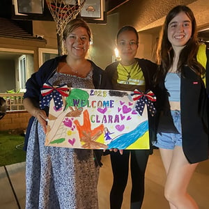 Alumnas de InterWay junto a su familia de acogida muestran sonrientes un colorido cartel de bienvenida personalizado con huellas de manos.