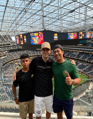 Tres estudiantes del programa de InterWay posan en la zona alta de las gradas de un inmenso estadio cubierto durante una excursión.