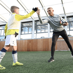 Un joven portero con equipación amarilla practica el bloqueo del balón con las manos junto a su entrenador en el curso de fútbol en Londres de InterWay.