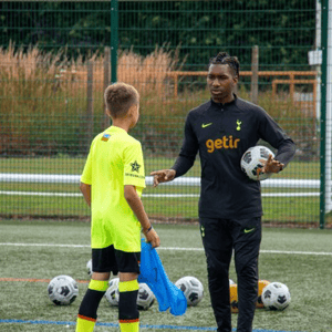 Un alumno con peto amarillo recibe las pautas de un monitor deportivo durante una sesión técnica individual de fútbol en el programa de InterWay en Londres.