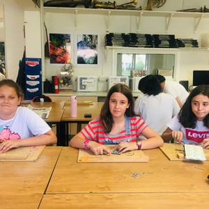 Alumnas del programa Hurst College Kids de InterWay concentradas durante una actividad de taller manual en una mesa de madera en el aula