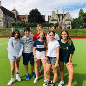 Un grupo de niños y niñas posando sonrientes en las zonas verdes exteriores frente a los edificios históricos del campus de Hurst College con InterWay