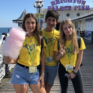 Tres jóvenes alumnos de InterWay con camisetas amarillas del programa sosteniendo un algodón de azúcar frente a la entrada del Brighton Palace Pier.