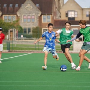 Jóvenes adolescentes jugando un partido de fútbol con petos en un campo de césped artificial exterior de Hurst College con InterWay.