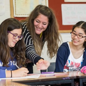 Una profesora sonriente guía a dos alumnas durante una actividad interactiva dentro de las aulas del curso Hurst College Teens de InterWay.