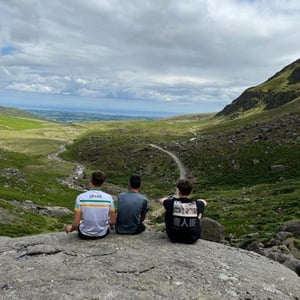 Tres jóvenes estudiantes del curso de InterWay sentados en una roca contemplando un inmenso valle verde bajo el cielo irlandés.