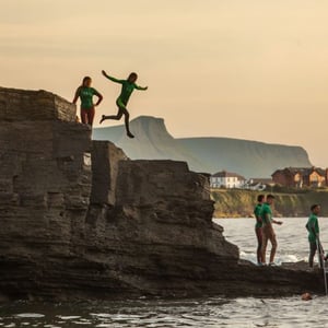 Alumnos del programa de verano de InterWay saltando al agua desde un acantilado bajo la luz del atardecer en Irlanda.