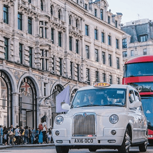 Un típico taxi blanco londinense y un autobús de dos pisos rojo circulando por las calles de Londres durante una excursión del programa de InterWay.