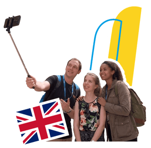 Tres estudiantes de InterWay sonriendo mientras usan un palo selfie durante su curso de inglés en Londres, con la bandera del Reino Unido y elementos de marca amarillos sobre fondo oscuro.