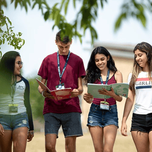 Cuatro estudiantes jóvenes del curso de verano de InterWay caminando y sonriendo mientras revisan sus materiales académicos al aire libre en Londres.