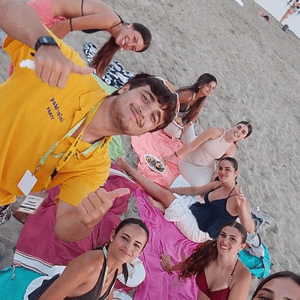 Un monitor con camiseta amarilla de InterWay haciéndose un selfie con un grupo de estudiantes sentados sobre toallas en la arena durante un picnic en la playa de Malta.