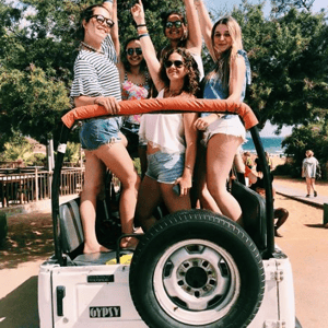 Estudiantes del curso de verano de InterWay saludando divertidos de pie a bordo de un jeep blanco durante una excursión de aventura por Malta.
