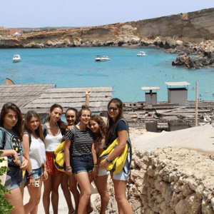 Estudiantes del programa de idiomas de InterWay posando junto a una cala de aguas cristalinas de color turquesa en la isla de Comino, Malta.