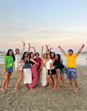 Grupo de estudiantes del curso de inglés en Malta de InterWay posando divertidos y con los brazos en alto en la arena de la playa durante el atardecer.