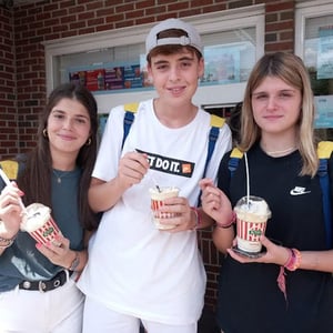 Tres jóvenes estudiantes del viaje de InterWay disfrutan de una merienda y sonríen en el exterior de un establecimiento comercial en EE. UU.