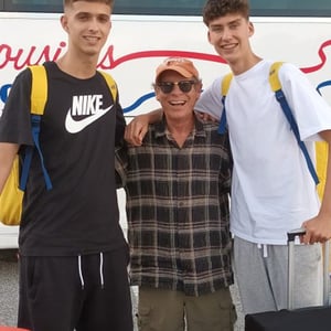 Dos alumnos del programa de verano de InterWay posan en una calle residencial abrazando cariñosamente a un miembro de su comunidad anfitriona americana.